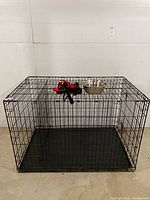 Full view of black wire dog crate with attached metal bowl and leashes on top, showing size and general structure