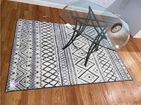 Full view of the gray and white geometric patterned area rug under a glass table on hardwood floor, showing overall design and shape.