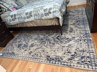 Photo showing the full rug placed under bed, exhibiting blue, grey, and off-white pattern and size.