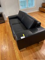 View of the black leather-like sofa from an angle, showing the seat cushions, armrest, and back cushions.