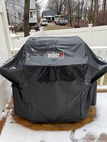 Grill fully covered with black Weber protective cover on deck.