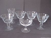 Photo shows six assorted vintage crystal cocktail glasses: four with etched bird design on bulbous bases, two with slight chips; one shallow glass with etched floral and X-shaped design; one tall narrow glass with etched bird design.