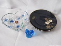 Photo showing the three blue glass items: heart-shaped dish with blue flowers, dark blue gold-rimmed plate with gold floral design, and small blue glass bird figurine.