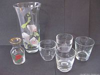 Image showing all glassware items arranged against a dark backdrop: large floral decorated crystal vase, small gold-rimmed decanter/vase, four assorted drinking glasses.