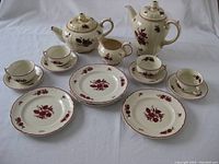 Full set showing tea pot, coffee pot, creamer, sugar pot, cups, saucers, and dessert plates with burgundy floral hand-painted pattern on white porcelain.