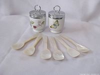 Photo showing the pair of Royal Worcester egg coddlers alongside six mother-of-pearl egg spoons on a white background.