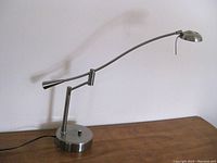 Side view of the large metal desk lamp fully extended on wooden surface against white wall.