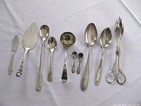 Full set of 9 pieces of sterling silver and silver-plated tableware including spoons, ladle, salad tongs, cake server, and butterknife laid out on white cloth