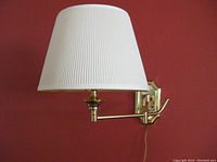 Vintage wall-mounted brass lamp with white ribbed shade mounted on red wall, shown extended with shade visible.