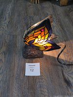 Side and front view of butterfly stained glass lamp showing warm light inside, wired cord attached, and small damage to wire frame at front edge.