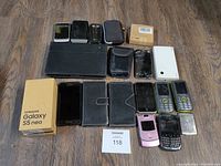 Top down view of all phones and accessories laid on wooden floor including Samsung Galaxy S5 Neo box, multiple smartphones, flip phone, and phone cases