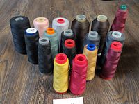 View of 17 partial spools of thread arranged on wooden floor, varying colors and spool sizes.
