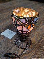 Close-up image of goblet-shaped Tiffany style stained glass lamp with rich colors and ornate metal base on wood surface.