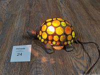 Front-side view of turtle lamp illuminated on wood floor with MaxSold card