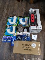 Lot overview showing four white PVC J-bend pipes with blue caps, a red pipe cutter in packaging, a metal can, a small container, several fittings and adapters in blister packs, and a boxed refrigerator automatic ice maker kit.
