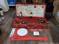 Closed red steel toolbox with Milwaukee Right Angle Drive Drill Accessories label inside lid and various accessories inside, including auger bits and extensions.
