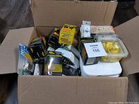 Box of assorted electrical supplies including multiple boxes of 40W light bulbs, power outlets, and yellow wire connectors.