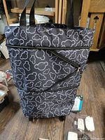 Front view of folding shopping cart in black fabric with white Mickey Mouse head patterns. Shows carry handles and zippered sections.
