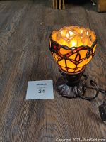 Front angled view of illuminated goblet stained glass lamp on wooden floor, showing amber glow and red jewel accents.