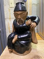 Front view of hand painted clay statue showing facial details, black attire, and seated pose.