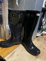 Side angle view showing the left and right boots standing on a wooden surface, with visible adjustable buckle on the side of one boot.