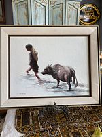 Framed oil painting showing man and water buffalo walking through water, signed by artist.
