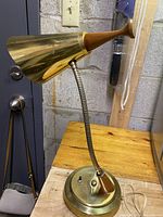 Front view of vintage desk lamp showing brass conical shade, wood accent, and base with toggle switch on wooden surface against block wall.