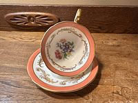Top-down photo showing the cup resting on the saucer, highlighting the floral bouquet inside the cup and the gold detailing on both pieces.