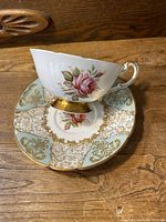 Cup showing pink rose design, gold leaf on foot, and curved handle with gold trim