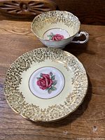 Photo showing the tea cup and saucer together on a wooden surface, highlighting the dark red rose in the center and delicate gold edging.