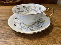 Side view of the cup resting on the saucer, showing the gold leaf floral decoration, gold trim, and ornate cup handle.
