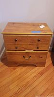 Front view of a wooden nightstand with two smaller upper drawers and one large lower drawer, showing worn finish and hardware details.