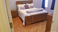 Ashley queen bed frame set up with bed linens and pillows to show style and condition. Medium brown wood with metal decorative accents on the headboard.