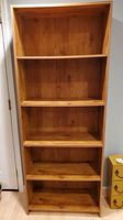 Front view of the tall, medium brown wood grain bookcase showing all four shelves and base with visible wear marks.