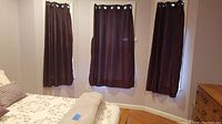 Three dark-colored curtains hung on windows in bedroom, medium length, metal grommet hangers visible