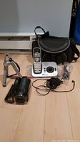 Sony Handycam, mini tripod, carrying case, power cords, and Uniden cordless phone with answering system base unit arranged on floor.