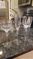 Three Lenox stemware glasses with gold rims shown on a kitchen countertop with varying styles and twisted stems.