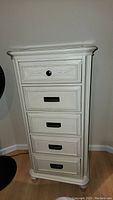 Front view of a tall white lingerie dresser with five drawers, showing one knob and four handles.