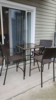Full view of patio bistro set on concrete patio with glass top table and three chairs showing general condition, matching chairs and seating style