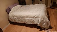 Full double bed made with comforter, pillows, and sheet in a bedroom with wooden floor