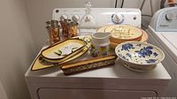 Photo showing full set of ceramic serving dishes, copper cups, glass decanter, and plates arranged on a dryer