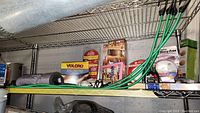 Metal shelving with various packaged smoke detectors, adhesive supplies, and cooking mats, showing a general overview of the items in the lot.