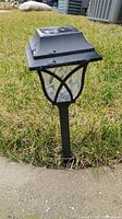 First solar outdoor garden light installed in grass next to concrete.