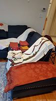 Wide view of couch with multiple oblong tablecloths in floral, cream/eucalyptus, and burnt orange colors, some folded and draped.