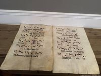 Two large vellum sheets featuring illuminated Latin chants, musical notation in black squares on red staves, and gothic script with visible wear.