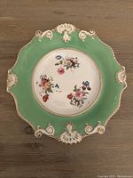 Top view of antique ceramic plate showing green rim with white ornate decorations and central floral pattern.