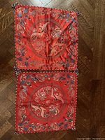 Pair of red silk pillow cases featuring circular embroidered dragon and phoenix designs with floral and geometric patterns, shown laid flat on wood floor.