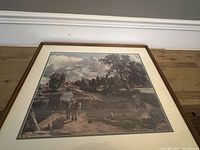 Framed print of a rural landscape scene with horse near a river and background houses