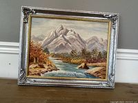 Framed oil on board landscape painting with decorative silver frame and gold inner edge shown at a slight angle.