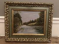 Framed oil on board painting showing river and trees with signature visible on lower right.